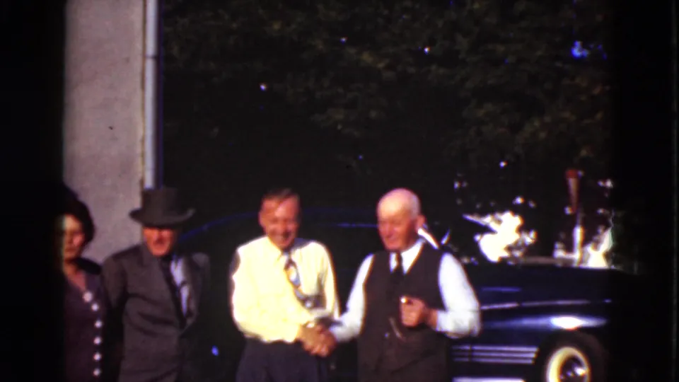 The closing Denmark 1975 frame holds on the handshake, with the adults smiling near a building edge and dark vintage car.