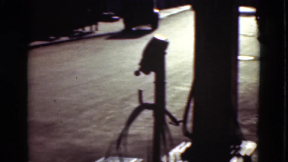 1975 Denmark 8mm frame showing a dark gas pump silhouette near a paved roadside, with strong shadowing and visible film gate edges.