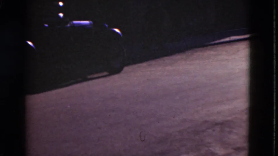 1975 Denmark 8mm frame with a paved street surface and the front portion of a parked car partly visible at the top edge.
