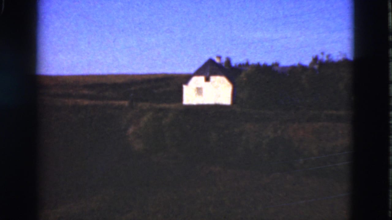 Small white house on a grassy hill beneath a blue sky.
