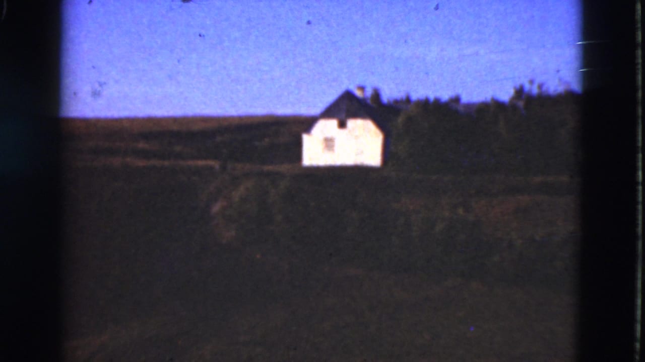 Distant white house beside trees in open countryside.