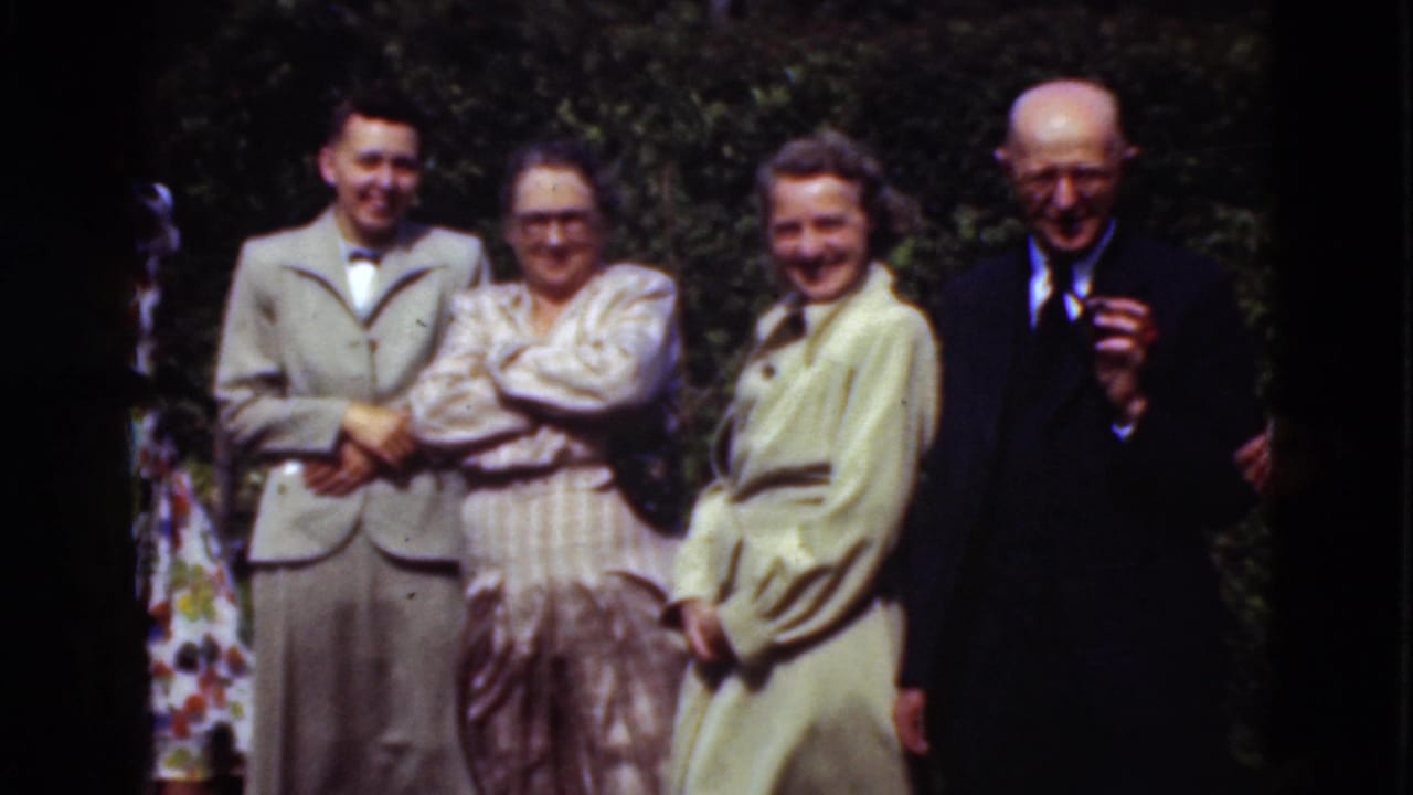 Five adults stand close together outdoors, including an older man in a dark suit.