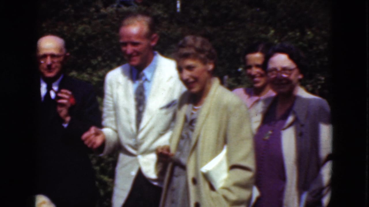 A 1975 Denmark home-movie frame shows a smiling group walking through a sunny outdoor setting in formal clothes.