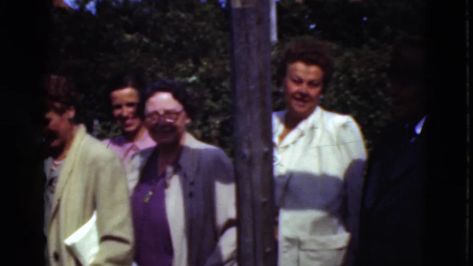 The later frame shows women in light-colored formal clothing and other adults near a post in a sunny Denmark outdoor setting.