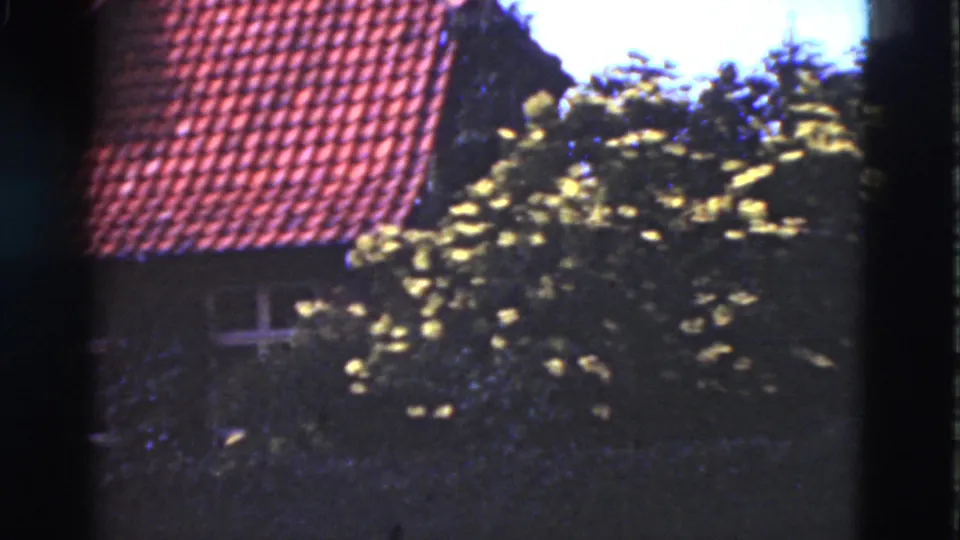 1975 Denmark 8mm frame showing a red tiled house roof, dark facade, white-framed window and leafy foreground branches.