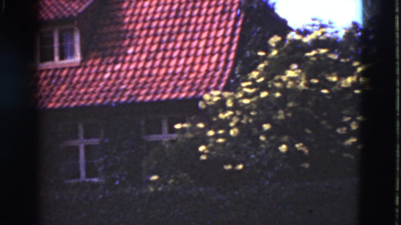 1975 Denmark 8mm frame with a red tiled roof, small dormer, white-framed windows and dense foliage in front of the facade.