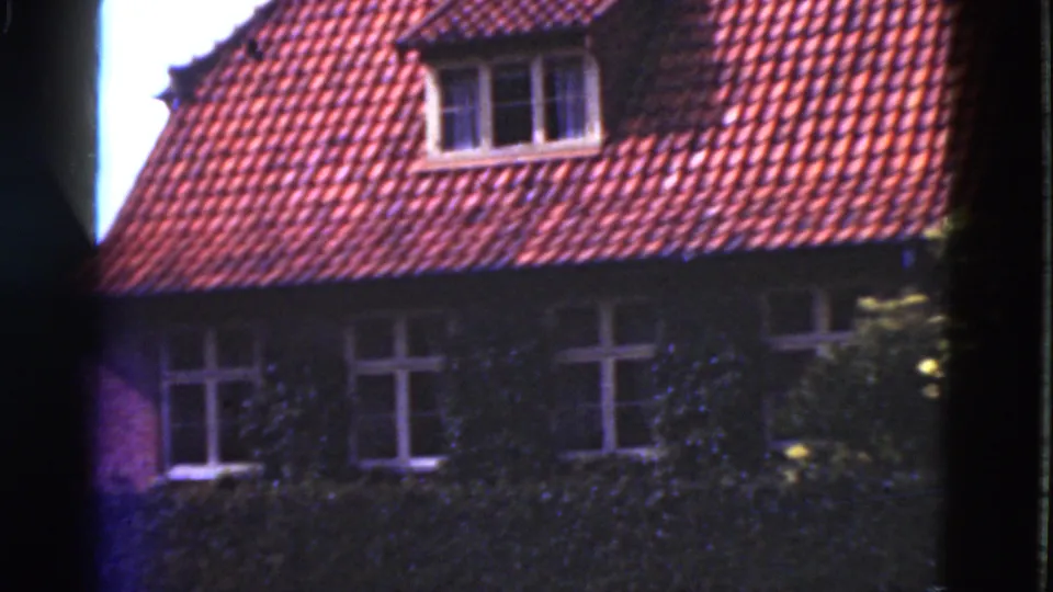 1975 Denmark 8mm frame showing a broad view of the red roof, dormer, ivy-covered facade and multiple white-framed windows.