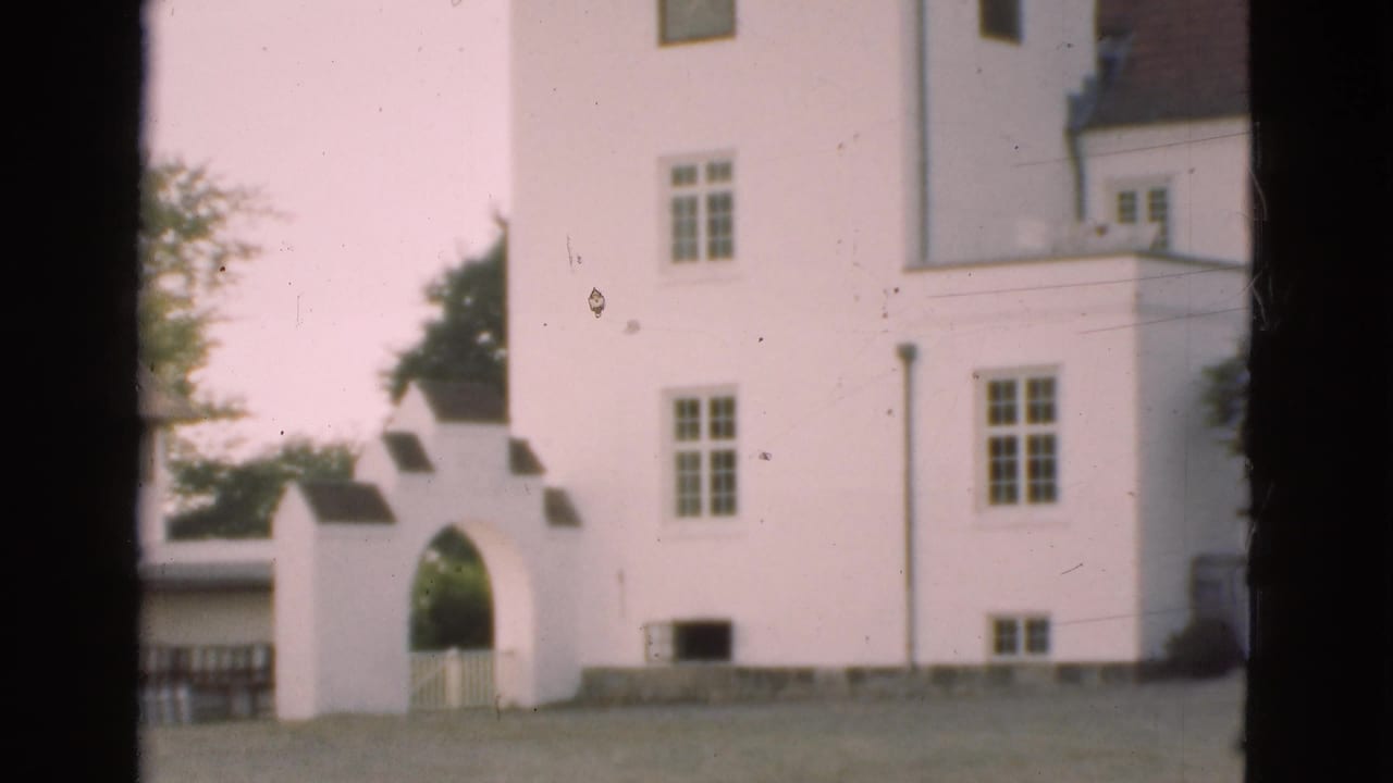 White historic building with arched gateway, lawn, windows, and dark film-frame edges.