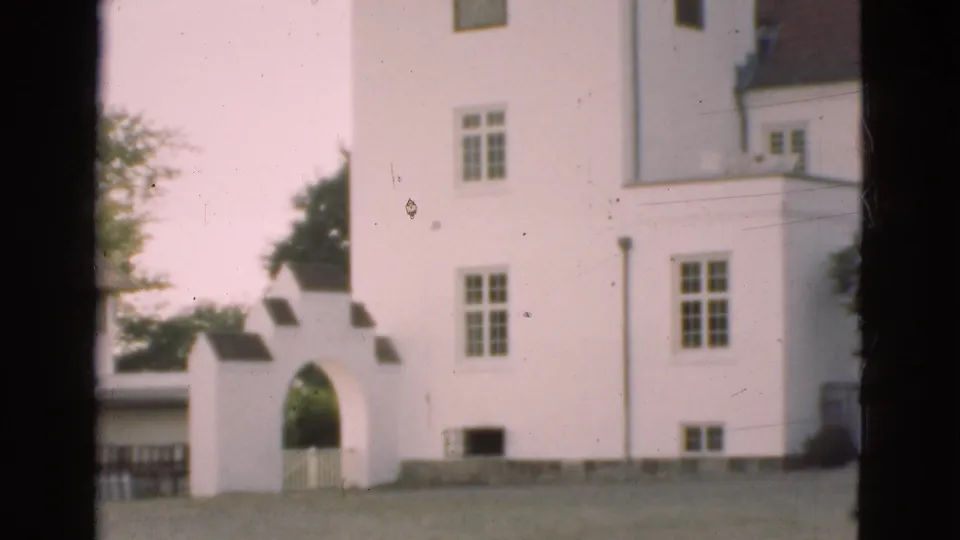 1975 Denmark 8mm frame showing a white historic building facade, arched gateway, lawn, and dark scan borders.