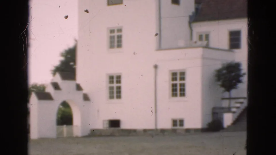 1975 Denmark 8mm frame with a white building, arched entrance, windows, roof sections, trees, and visible film wear.