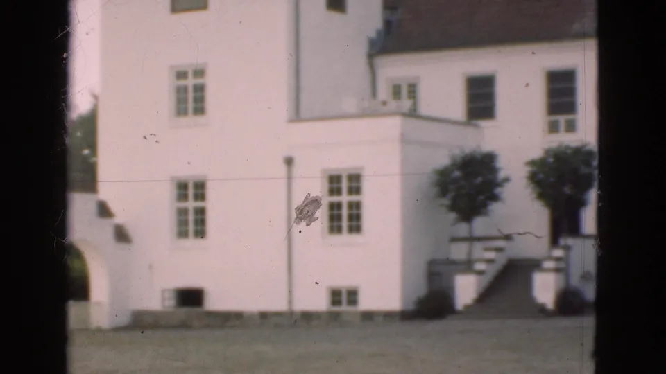 1975 Denmark 8mm frame showing the white building from closer range, with windows, part of an archway, stairs, and lawn.