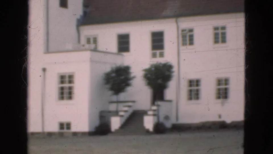 1975 Denmark 8mm frame showing a white multi-storey building across an open foreground, with stairs, windows, and small trees near the entrance.