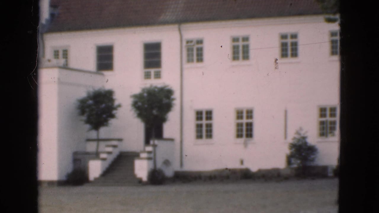 White building facade with rows of windows, entrance stairs, small trees, and open ground in front.