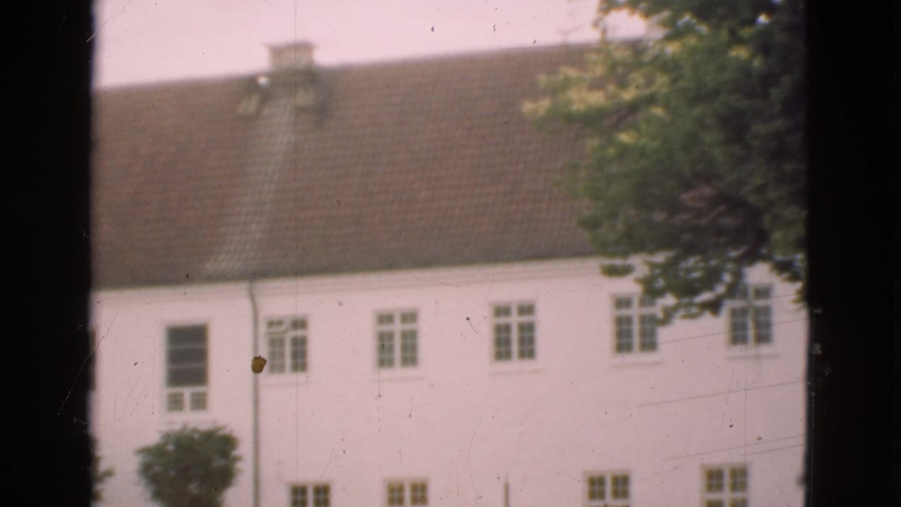 White multi-story building with brown tiled roof seen through dark window framing.