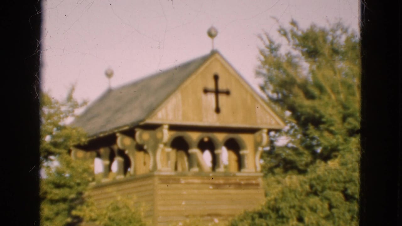 1975 Denmark 8mm frame of a wooden church tower with a black cross, arched openings, carved supports, and surrounding trees.