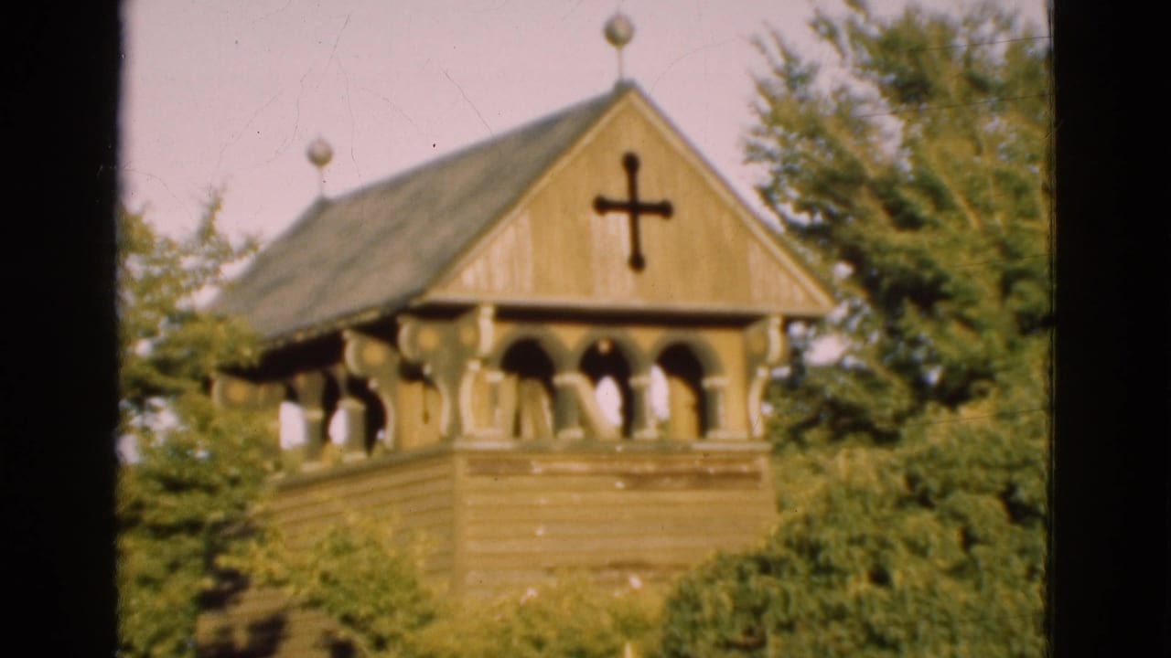 1975 Denmark 8mm frame showing the church tower roof, black cross, decorative finials, arched openings, and green trees.