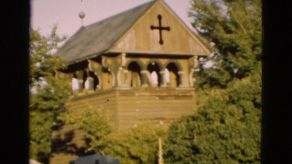 1975 Denmark 8mm frame as the pan moves down from the wooden church tower toward shrubs and a grave marker.