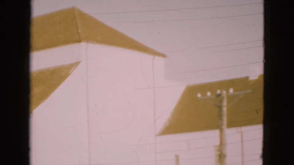 1975 Denmark 8mm frame showing white buildings with brown pitched roofs, pale sky, and a dark window-frame edge.