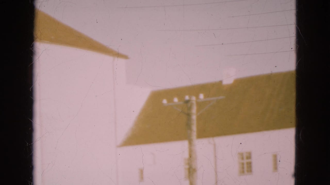 1975 Denmark 8mm view of a utility pole and overhead lines against white buildings with brown sloped roofs.