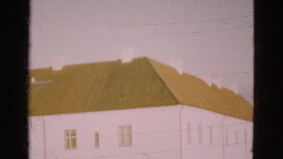1975 Denmark 8mm frame showing a longer white building with brown roof sections, small windows, and faint power lines.