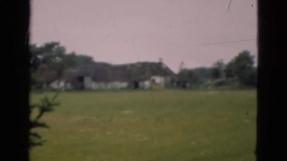 End frame of the 1975 Denmark countryside view, showing a thatched cottage across pasture through dark window-like framing.
