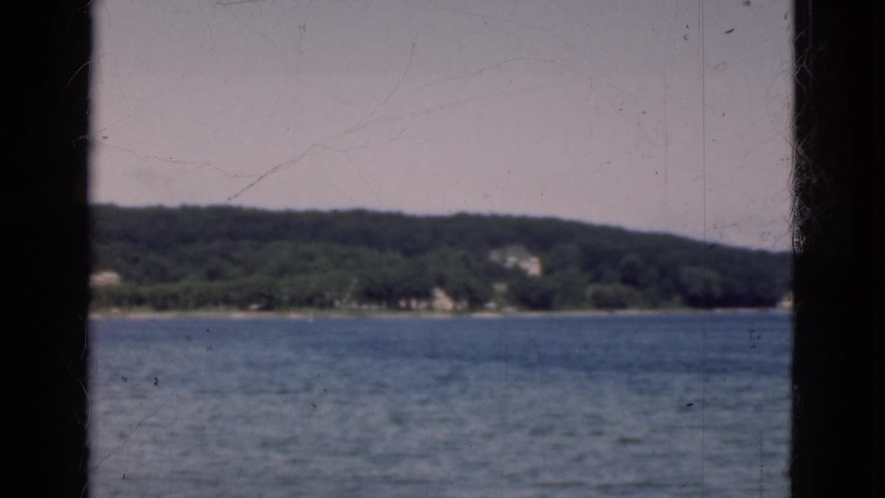 Rippling lake seen through dark vertical framing with a wooded shoreline in the distance.