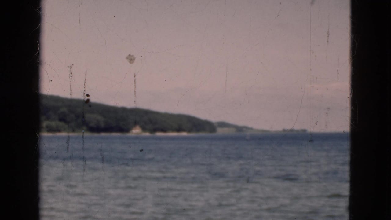 Water view with wooded shoreline and distant hills framed by dark film borders.