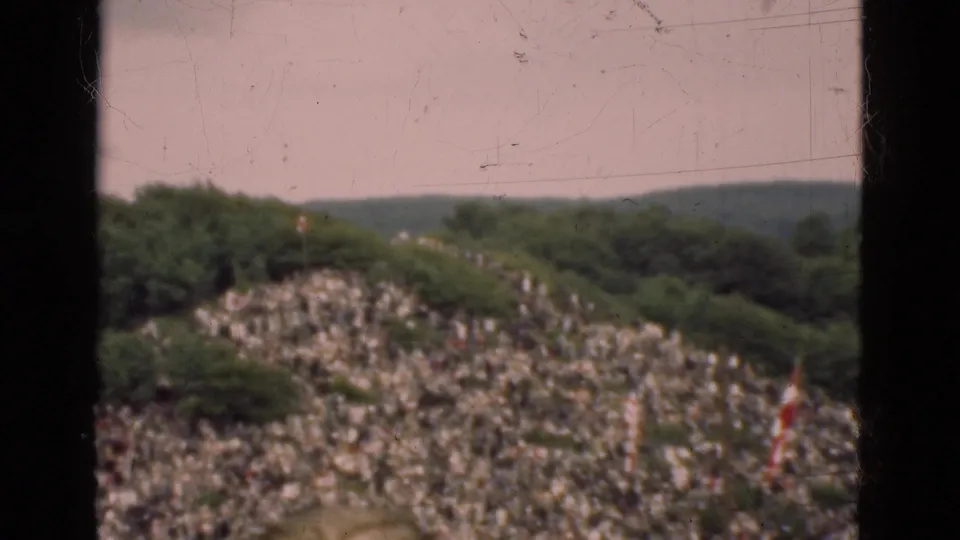 1975 Denmark 8mm frame showing a wooded hillside and many distant people gathered along a sloped area.