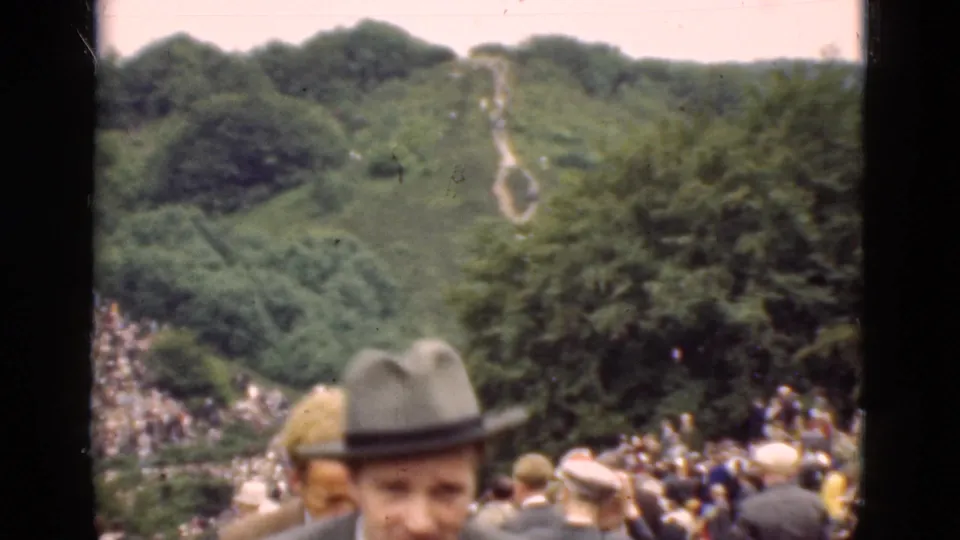 1975 Denmark frame showing foreground spectators, a large hillside crowd, trees, and a pale path across the slope.
