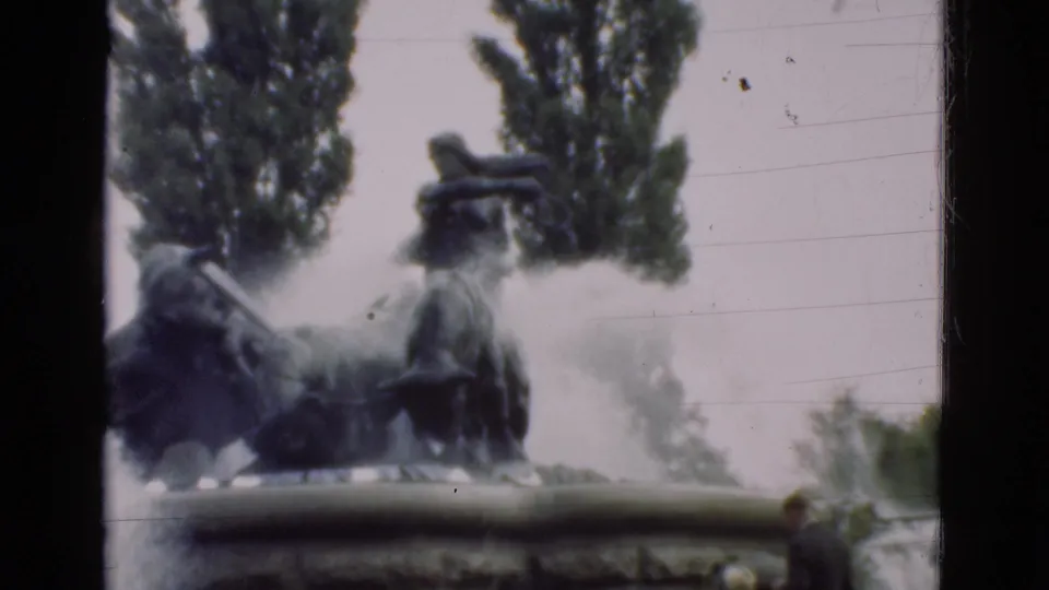 The final frame centers the dark fountain sculpture and misting water, with a partial visitor visible near the lower edge of the park scene.