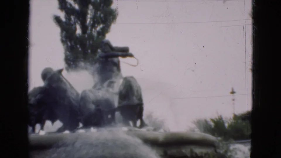 A bronze sculptural fountain with figures on horseback is seen through soft 8mm focus and water spray in the Denmark home-movie clip.