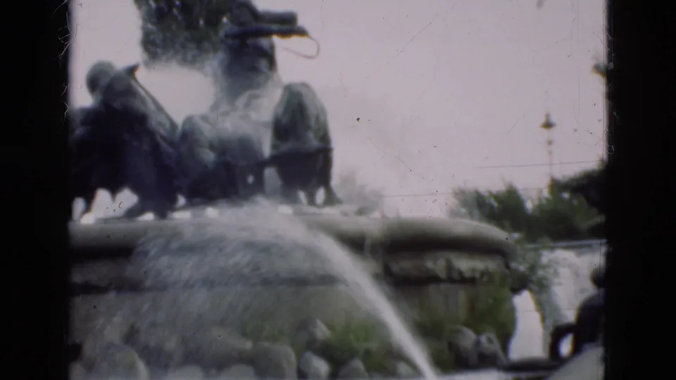 The closing frame centers the gushing sculptural fountain, with bronze horse-mounted figures, stone basin edges, and nearby greenery visible.