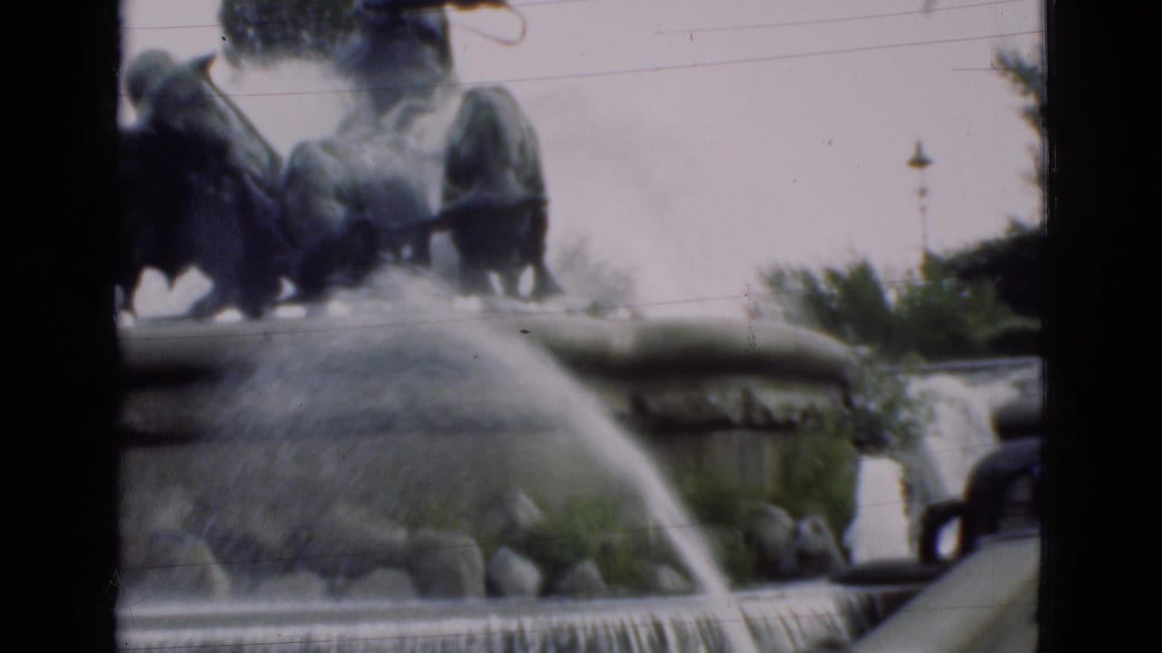 Tiered fountain with water arcing over rocks and dark sculptural forms above the basin.