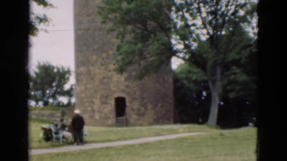1975 Denmark park scene with a tall round stone tower, grass lawn, trees, benches, and distant visitors in casual clothing.