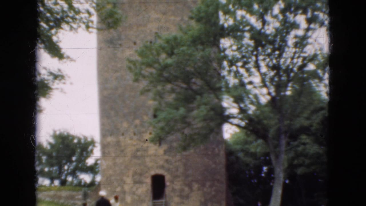 Stone tower partly framed by trees and dark film borders, with small visitors near the base.