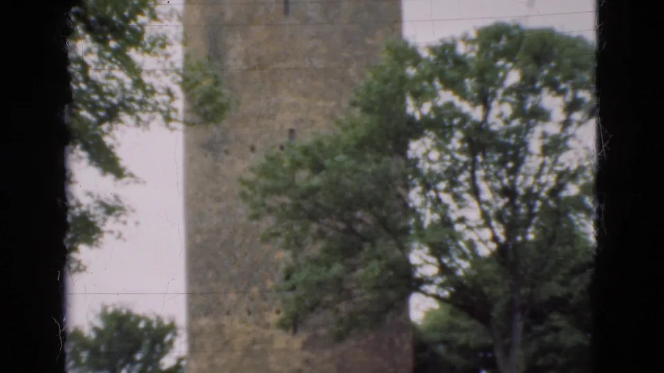 1975 Denmark 8mm frame with a weathered stone tower, leafy trees, pale sky, and heavy dark borders from the film scan.
