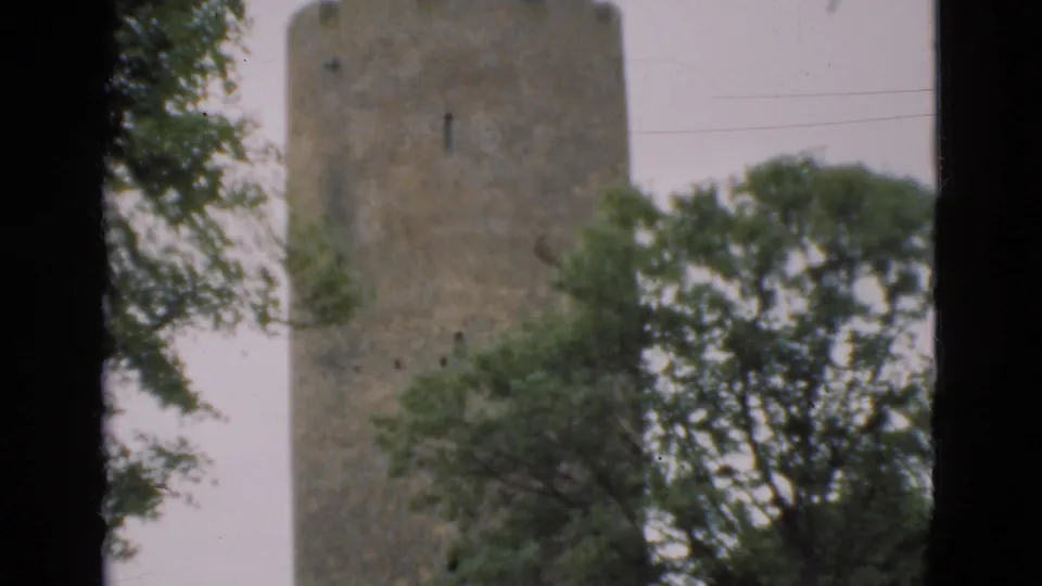 1975 Denmark 8mm frame showing the upper stone tower through trees, with soft focus, grain, and dark frame edges.
