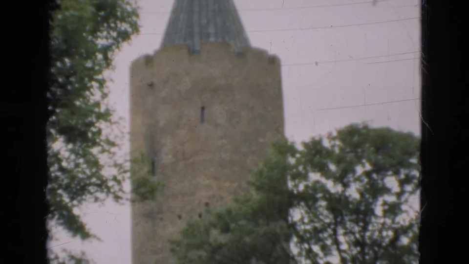 1975 Denmark 8mm frame showing the top of a round stone tower with a conical roof, trees, pale sky, and film borders.
