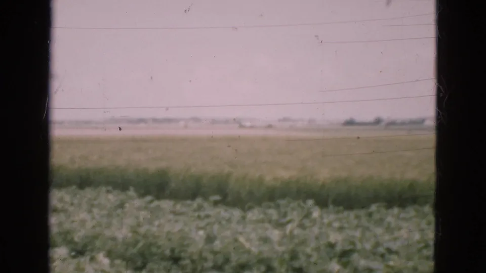 A Danish rural field appears beyond a dark window frame, with faded color, light scratches, and a soft distant horizon.