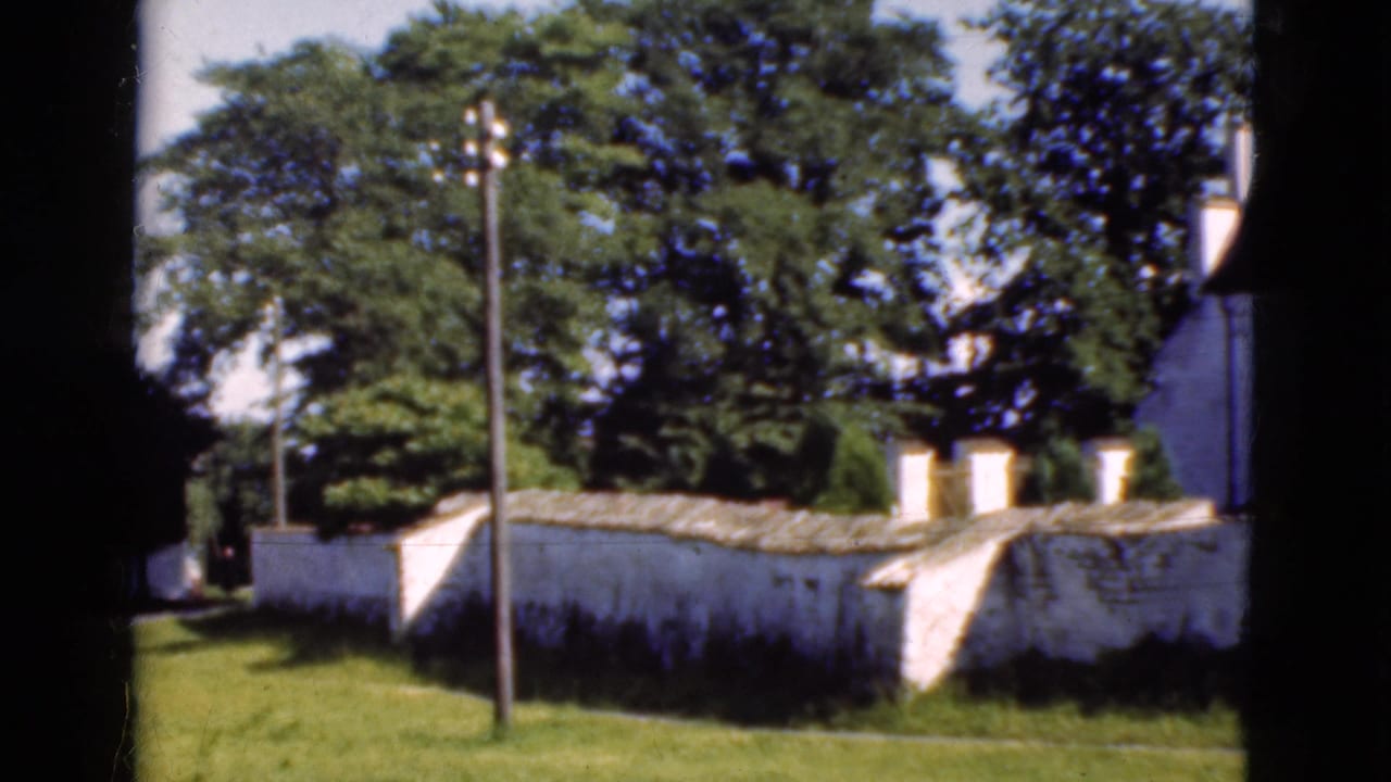 White stone wall and tall white building partly framed by trees and a utility pole.