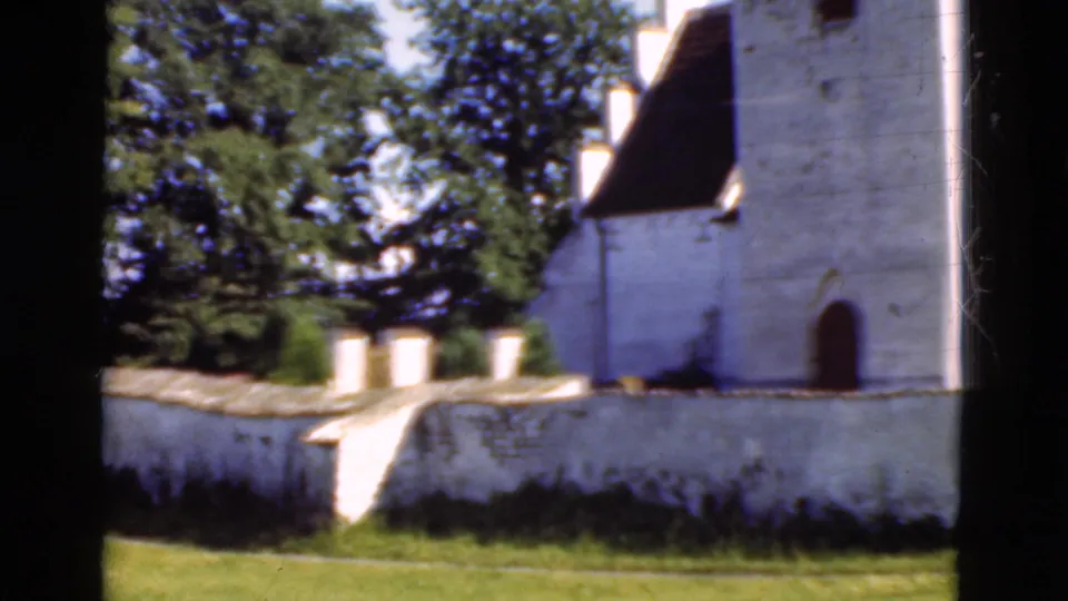 1975 Denmark home-movie frame with a tall white building, arched doorway, stone wall, trees, grass, and visible 8mm frame edges.