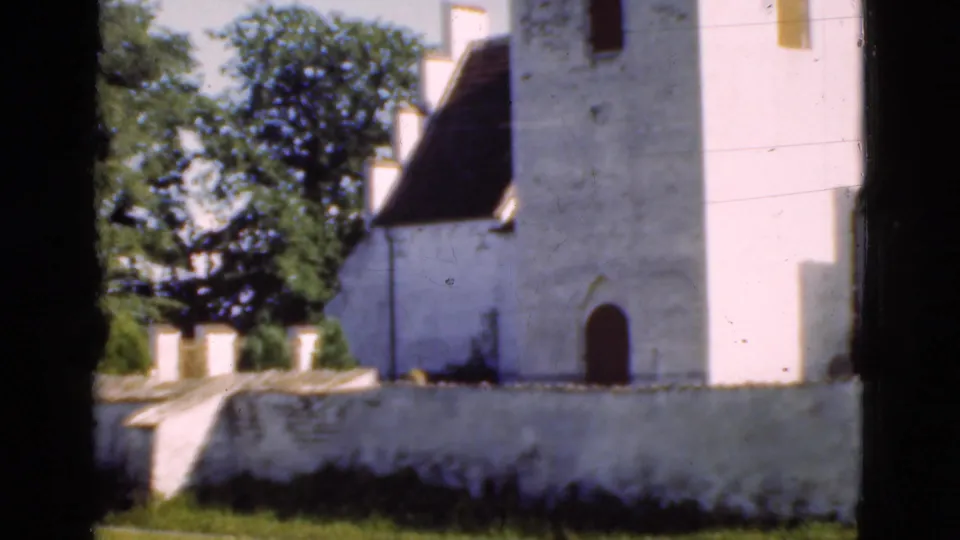 1975 Denmark frame with the white church tower, steep roof, trees, low wall, and arched doorway partly visible.