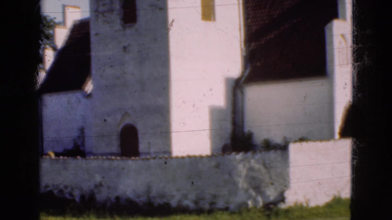 1975 Denmark 8mm frame with the white church tower, red-tiled roof, arched doorway, low wall, grass, and central gate shadow.