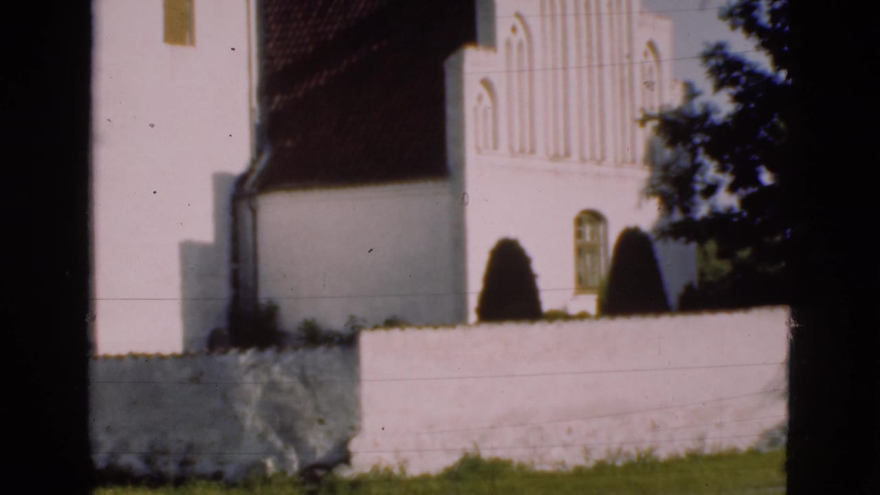White church wall and arched window partly obscured by tree branches.