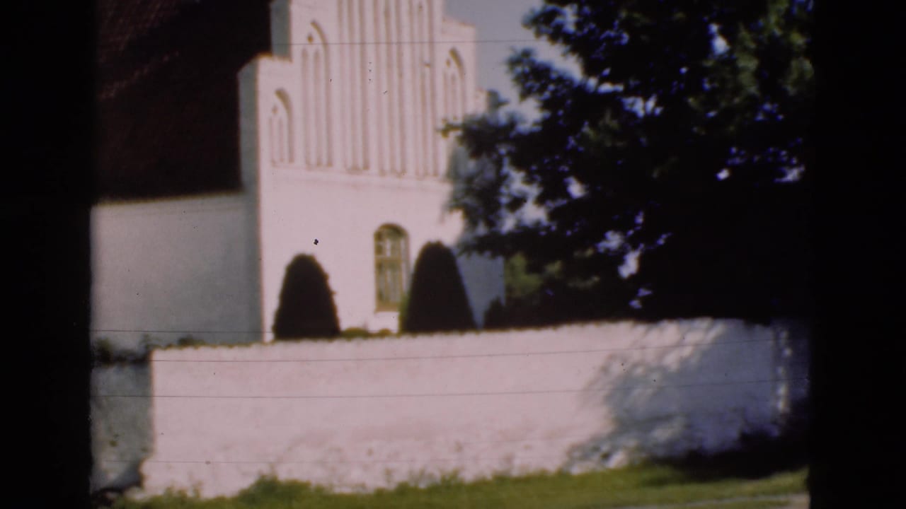 White church facade behind a low white wall, with trees and dark framing at the edges.
