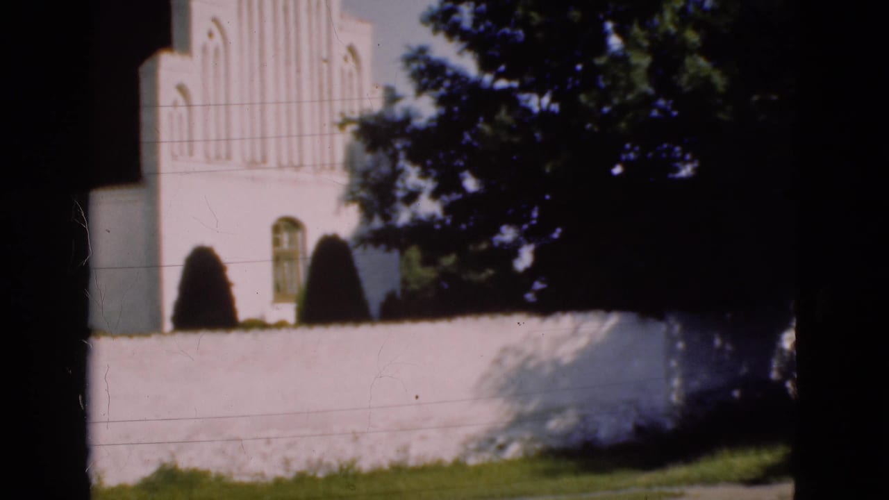 White church wall and facade with shrubs, trees, grass, and dark vertical framing.