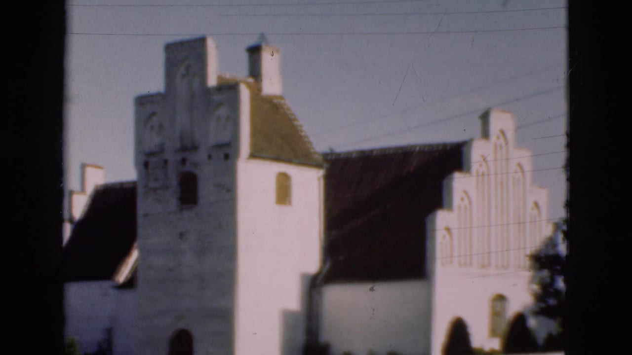 1975 Denmark 8mm frame showing a white church exterior with a tower, stepped gable, arched openings, and dark roof.