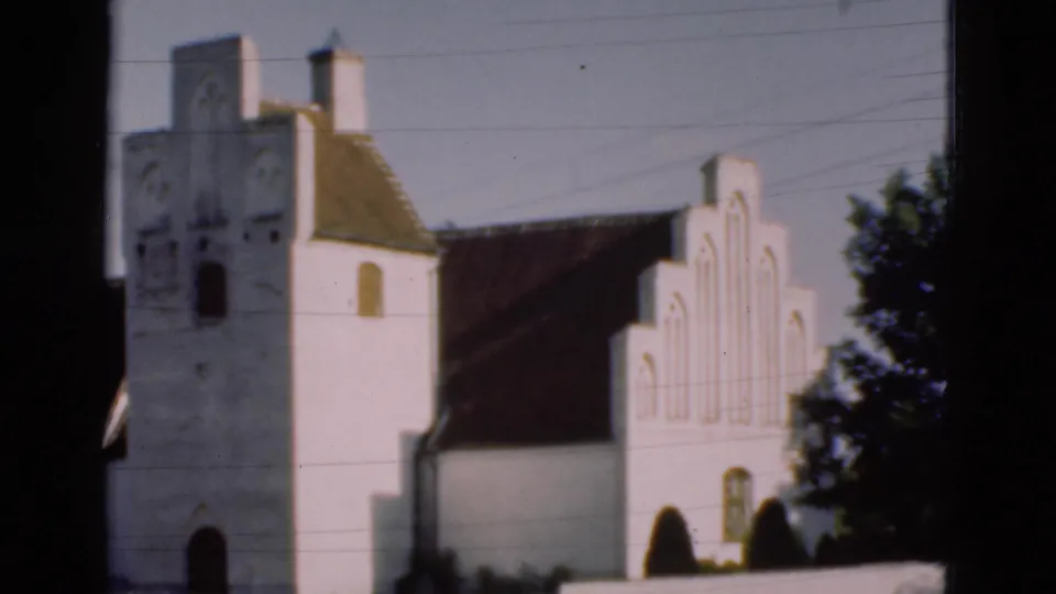 1975 Denmark 8mm frame of a white Gothic-style church exterior with a tower, stepped gable, dark roof, wires, and trees.