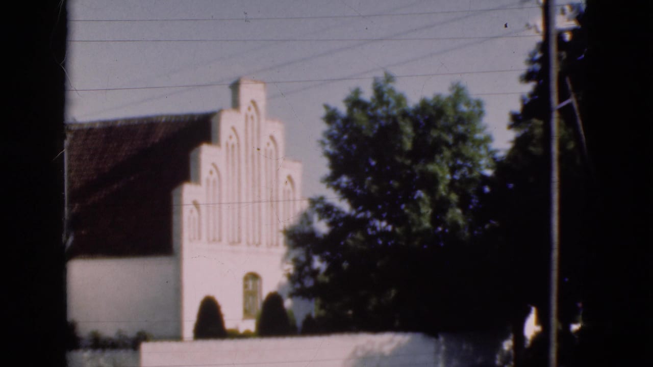 White stepped-gable building with arched window beside trees and a utility pole.