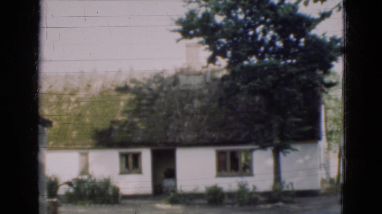 1975 Denmark 8mm view of a white thatched farmhouse, small windows, trees, shrubs, and dark window-frame borders.